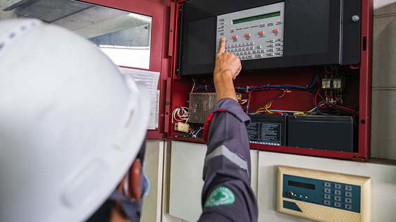 Technician in hard hat testing a fire alarm control panel for building safety system