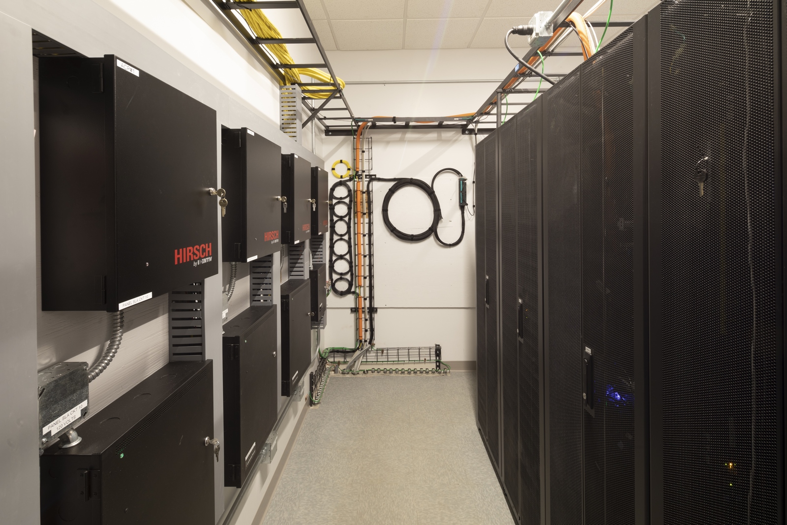 Server and telecom room with black equipment racks, Hirsch security panels, and organized cabling on wall and ceiling