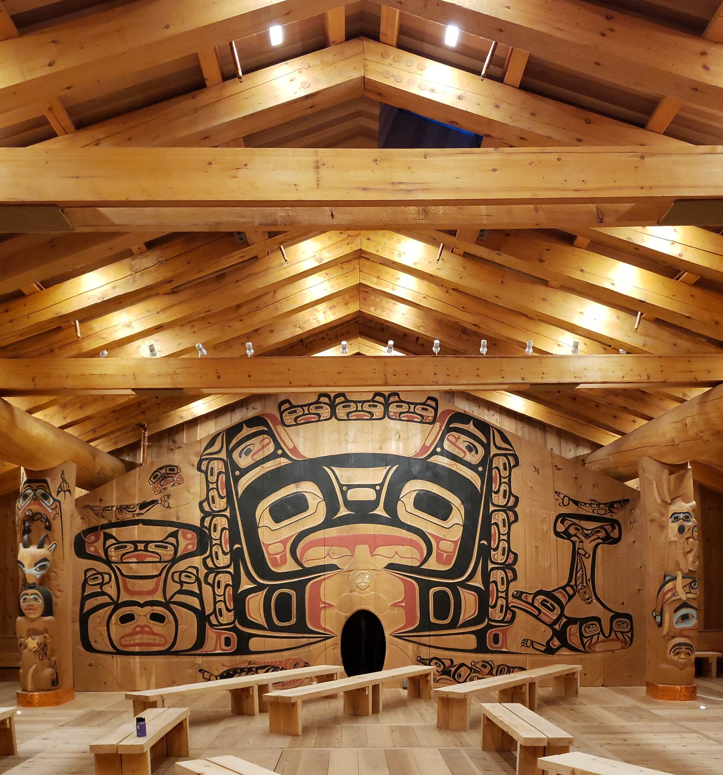 Traditional Alaska Native artwork painted on wood inside a timber-framed ceiling with spotlights