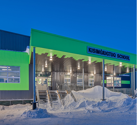 Kisimġiuqtuq School building with bright green trim and snow-covered entrance at dusk