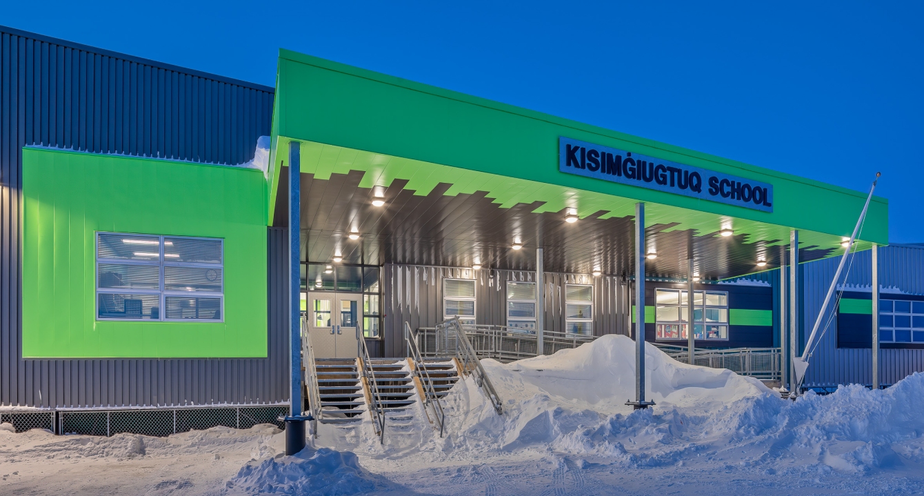 Kisimġiuqtuq School exterior with bright green entrance and snow-covered steps at dusk