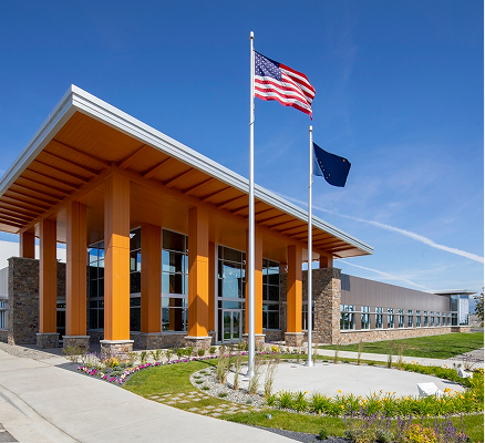 Modern building with tall glass entrance, orange columns, and U.S. and Alaska flags in front