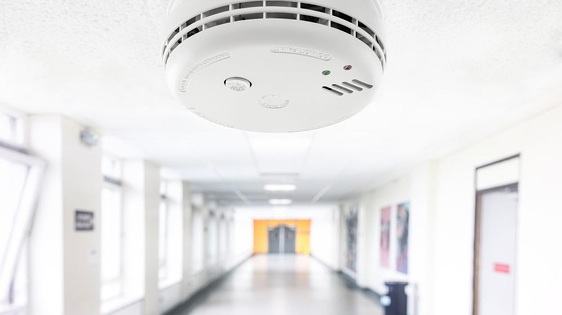 Smoke detector mounted on ceiling in a bright hallway for fire safety monitoring